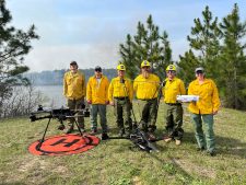 a group of people stand in front of a smoky natural area with the Alta-X drone