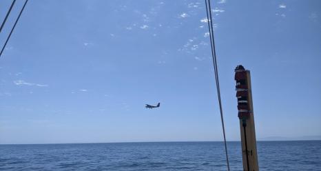 The Twin Otter research plane flies past RV Blissfully on sampling station. RV Blissfully’s surface light sensor is seen in the foreground. Photo by Bridget Seegers.